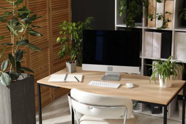 Modern bilgisayarı, kırtasiyesi ve çiçek dekoru olan şık bir iş yeri. Biyofilik iç tasarım