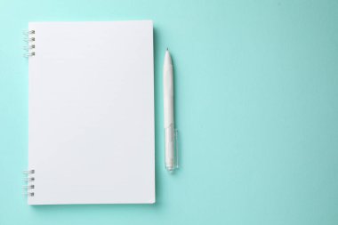 Açık mavi arka planda beyaz defter ve kalem, düz. Metin için boşluk