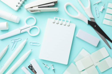 Açık mavi arkaplan üzerine beyaz defter ve diğer kırtasiye düz yatıyordu