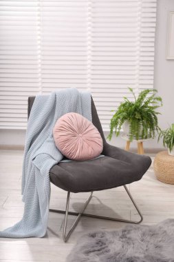 Oturma odasında pembe yastıklı ve battaniyeli rahat gri koltuk. İç tasarım