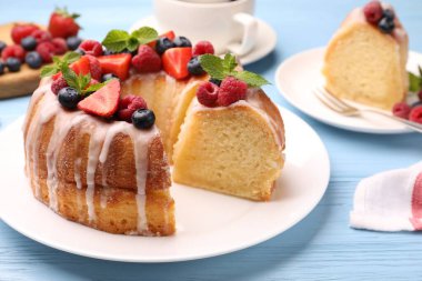 Lezzetli meyveli kek parçaları, açık mavi ahşap masa üzerinde jöle ve nane, yakın plan.