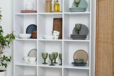 Farklı bulaşık takımları, bardaklar ve beyaz duvarın yanındaki diğer mutfak aletleri olan raf ünitesi.