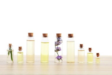 Beyaz arka planda, ahşap masanın üzerinde bitkilerle birlikte gerekli yağlar.