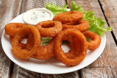 Ahşap masada soslu kızarmış kalamar halkaları, yakın plan.