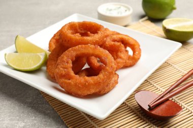 Kızarmış kalamar halkaları, limon, sos ve çubuklar gri masada, yakın plan.