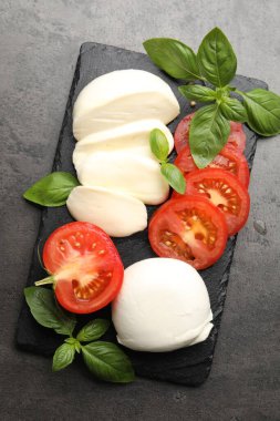 Lezzetli mozzarella peyniri, domates ve fesleğen gri masada, düz yerde.
