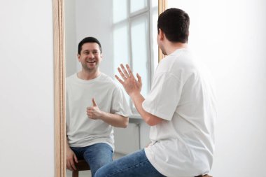 Aynanın önünde oturan bir adam. Aynadaki yansıması içeride parmaklarını gösteriyor. Ruh Sağlığı