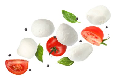 Mozzarella peyniri, domates ve fesleğen yaprakları beyaz arka planda uçuşuyor.
