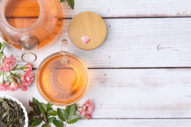 Cam fincanda nefis bir gül çayı, çaydanlık, çiçekler ve yapraklar açık ahşap masa üzerinde, düz uzanmış. Metin için boşluk