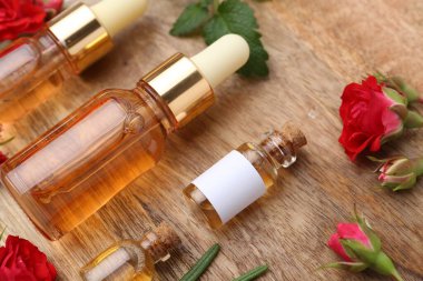 Gerekli yağlar, kırmızı güller ve ahşap masada bitkiler, yakın plan.