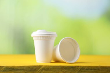 Tek kullanımlık plastik bardaklar sarı ahşap masada bulanık arka planda