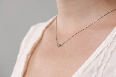 Açık gri arka planda şık bir kolye takan kadın, yakın plan.