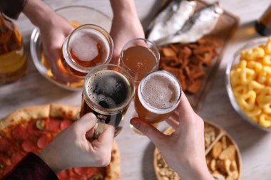 Arkadaşlar beyaz ahşap masada bira bardaklarını tokuşturuyor.