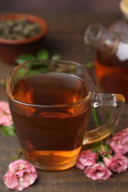 Cam fincanda lezzetli gül çayı ve ahşap masada çiçekler, yakın plan.