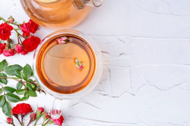 Cam fincanda romatik çay, çaydanlık, güller ve yeşil yapraklar beyaz masada, düz yerde. Metin için boşluk