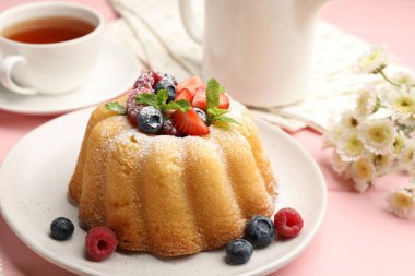 Pudra şekerli, böğürtlenli ve nane şekerli nefis kek, pembe ahşap masa, yakın plan.