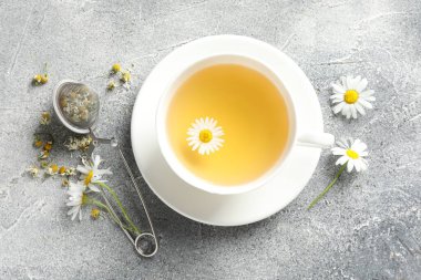 Lezzetli papatya çayı, zerk makinesi ve çiçekler açık gri masada, düz uzanmış.