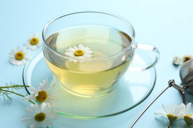 Lezzetli papatya çayı, aşılayıcı ve açık mavi arka planda çiçekler, yakın plan.