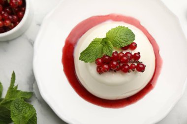 Kırmızı üzümlü lezzetli panna cotta, beyaz mermer masa üzerinde sos ve nane, düz yatıyordu.