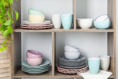 Beyaz duvarın yanında farklı bulaşık takımları, fincanlar ve çiçek dekoru olan raf ünitesi.
