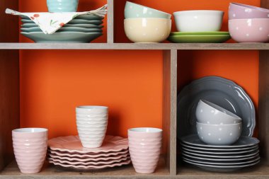 Kapalı alanda turuncu duvarın yanında farklı bulaşık takımları ve fincanlar olan raf ünitesi.