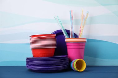 Tek kullanımlık plastik bulaşık takımı mavi ahşap masa üzerinde renk arkaplanına karşı