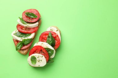 Mozarella peynirli lezzetli sandviçler, yeşil arka planda domates ve fesleğen, düz yatak. Metin için boşluk