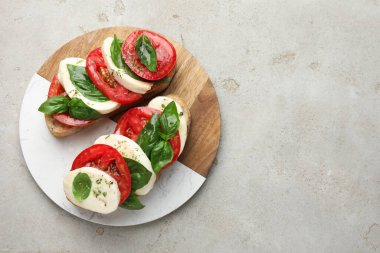 Mozarella peynirli lezzetli sandviçler, açık gri desenli masada domates ve fesleğen, üst manzara. Metin için boşluk