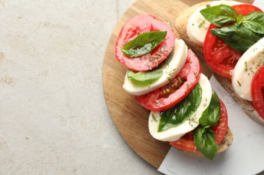 Mozarella peynirli lezzetli sandviçler, açık gri desenli masada domates ve fesleğen, üst manzara. Metin için boşluk