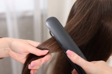 Kuaför kadın saçını düz ütüyle düzleştiriyor, yakın plan.