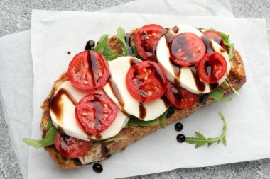 Mozarella peynirli lezzetli sandviç, balzamik sos, domates ve roka gri masada, üst görünümde.