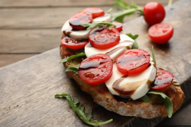 Mozarella peynirli lezzetli sandviç, balzamik sos, domates ve roka, ahşap masada, yakın plan. Metin için boşluk