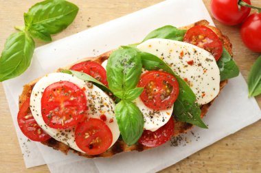 Peynirli, domatesli, ahşap masada fesleğenli lezzetli bir sandviç.