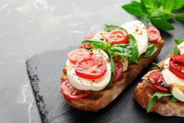 Mozarella peynirli lezzetli sandviçler, siyah mermer masada domates ve fesleğen, yakın plan. Metin için boşluk