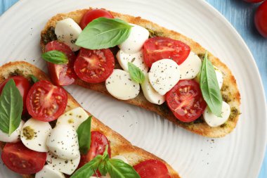 Peynirli, domatesli, açık mavi ahşap masadaki fesleğenli lezzetli sandviçler.