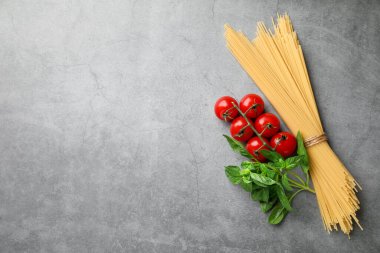 Çiğ spagetti makarna, domates ve fesleğen, gri desenli masa, düz yatak. Metin için boşluk