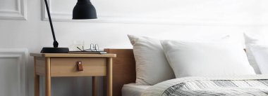 İçinde lamba, defter, bardaklar ve yatağın yanında bir bardak su olan komodin.