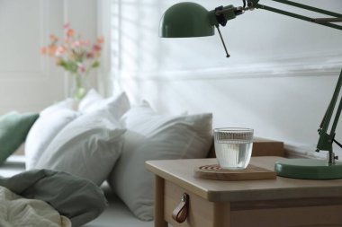 Yatak odasının yanında lamba ve bir bardak su olan komodin, yakın çekim.