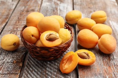 Hasır sepetin içinde taze kayısılar, ahşap masanın üstünde, yakın plan.