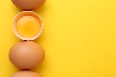 Sarı arka planda tam ve kırılmış tavuk yumurtaları, üst manzara. Metin için boşluk