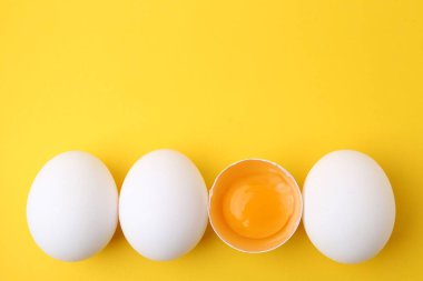 Sarı arka planda tam ve kırılmış tavuk yumurtaları, üst manzara. Metin için boşluk