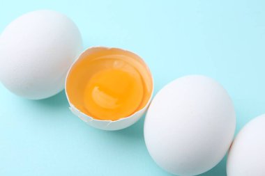 Açık mavi arka planda tam ve kırılmış tavuk yumurtaları, yakın plan.