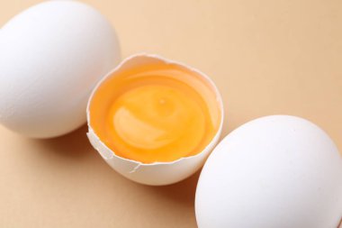 Bej arka planda tam ve kırılmış tavuk yumurtaları, yakın plan.