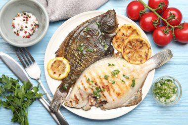 Açık mavi ahşap masada servis edilen limon dilimli ve otlu kızarmış balık. Ev yapımı deniz ürünleri yemeği.