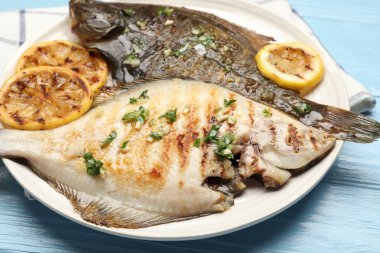 Açık mavi ahşap masa üzerinde limon dilimleri ve otlarla kızartılmış balık, yakın plan. Ev yapımı deniz ürünleri yemeği.