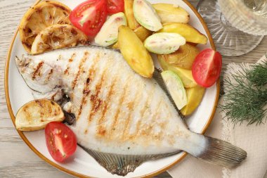 Hafif ahşap masada patates, domates ve limon dilimleriyle servis edilen kızarmış balık. Ev yapımı deniz ürünleri yemeği.