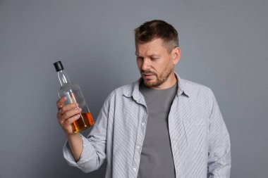 Gri arka planda akşamdan kalma viski şişesi olan bir adam.