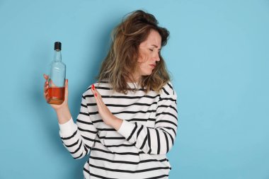 Bir şişe alkollü içki içen kadın açık mavi arka planda akşamdan kalma.
