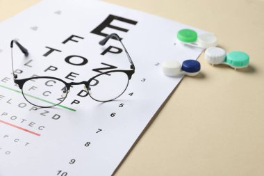 Vizyon test çizelgesi, bej arka planda gözlük ve lensler, yakın plan. Metin için boşluk