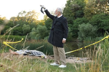 Adli tıp uzmanlığı. Cinayet mahallinde, göl kenarında cesetle birlikte çalışan bir dedektif.